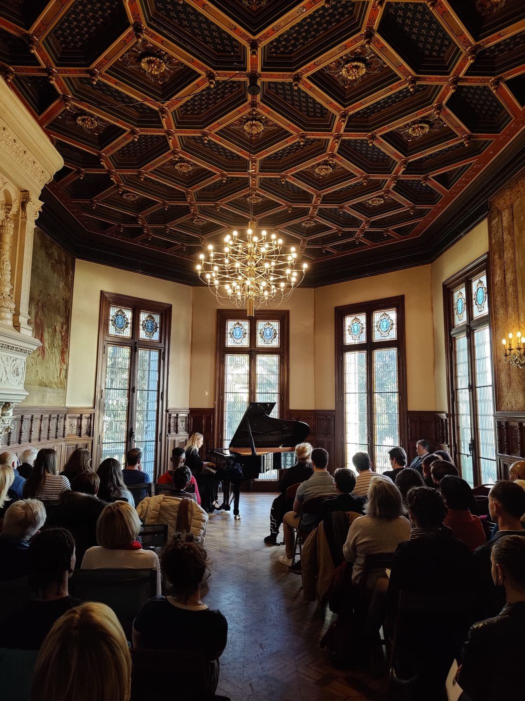 Le public assis devant le piano dans un salon à plafond à caissons